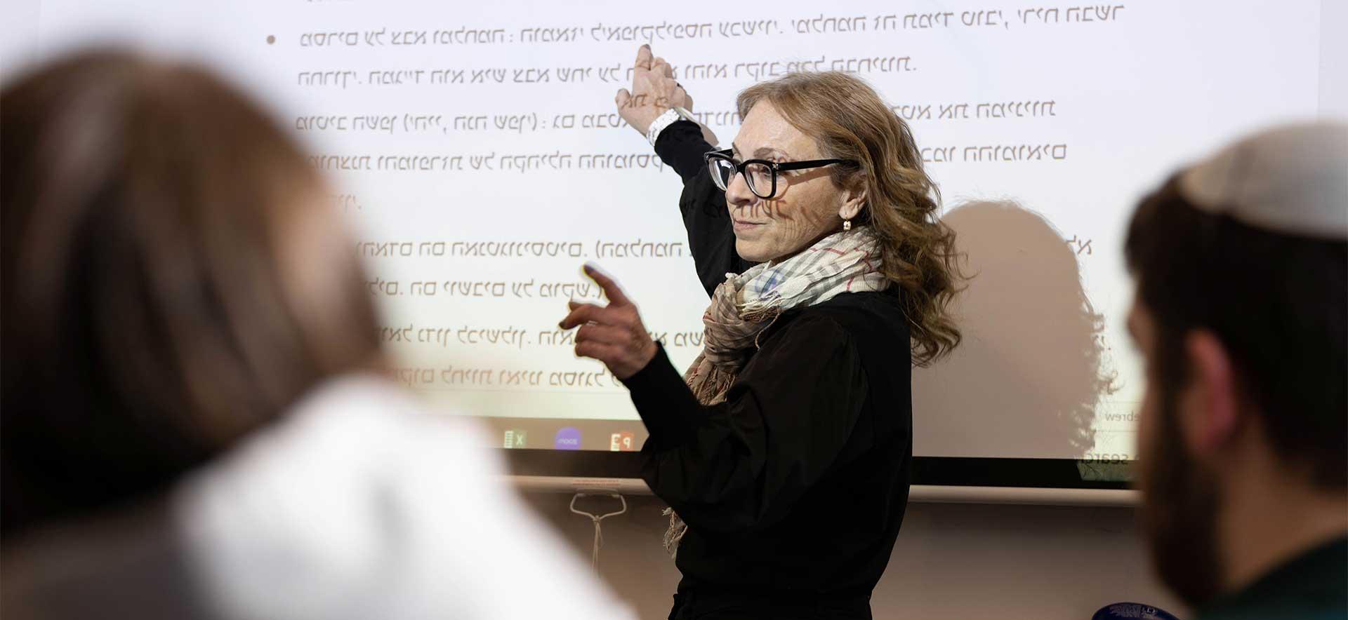 Professor Sara Hascal points to Hebrew projected onto a screen in a classroom